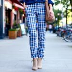 Le pantalon tartan femme pour booster votre style personne-portant-un-pantalon-tartan-debout-sur-un-trottoir-en-ville-entouree-de-facades-en-brique-et-de-cafes-details-visibles-comme-les-revers-du-pantalon-et-des-bottines-lumiere-douce-de-fi